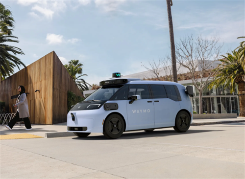 A light blue Waymo robotaxi on a city street, showcasing the next-gen vehicle model in its expanding service network.