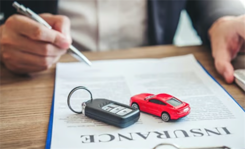 Person signing a car insurance policy document with a car key and model car, representing the link between EV safety and insurance costs.